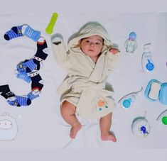 a baby in a bathrobe surrounded by toys and other items on a blanket