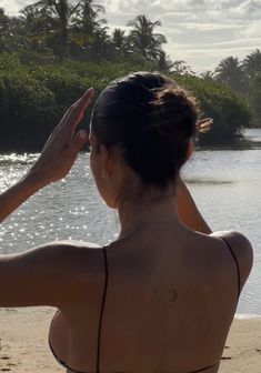 a woman standing on top of a sandy beach next to the ocean with palm trees in the background