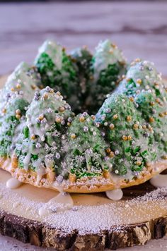 a green cake with white icing and sprinkles on it sitting on top of a piece of wood