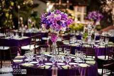 a tall vase filled with purple flowers sitting on top of a table covered in plates and silverware