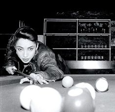 a woman leaning over a pool table with balls in front of her and an electronic device on the table