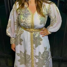 The "Rana" model is a Tlija type caftan in white and gold. It is a handmade kaftan, lined for more comfort and opacity on the body. The sleeves are transparent. Dress sold with its adjustable belt, its hanger and its protective cover. The model is wearing a size 38 which can also fit a size 36 because it is loose. Wedding Kaftan With Zari Work, Elegant Festive Dress With Intricate Design, Wedding Kaftan With Dabka For Transitional Season, White Kaftan For Wedding During Transitional Season, White Wedding Kaftan For Transitional Season, Festive Wedding Kaftan With Zari Work, Elegant Wedding Dress With Intricate Design, Elegant Floor-length Dresses With Intricate Design, Gold Dabka Kaftan For Wedding