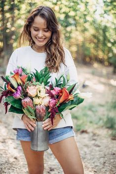 a woman holding a bouquet of flowers in her hands while standing on a dirt road