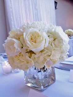 a vase filled with white flowers sitting on top of a table next to a candle