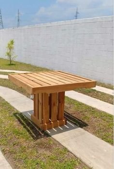 a wooden table sitting in the middle of a grass covered field next to a white brick wall