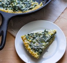 a slice of quiche on a plate next to a skillet with spinach