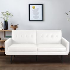 a white couch sitting on top of a wooden floor next to a shelf filled with vases