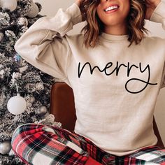 a woman sitting in front of a christmas tree wearing pajama pants and a sweatshirt