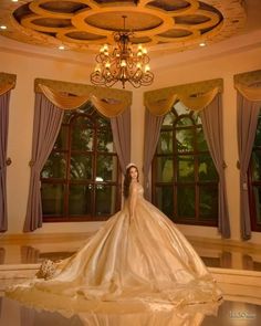 a woman in a wedding dress standing under a chandelier with curtains on the windows