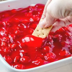 a hand dipping a cracker into a bowl of cranberry sauce