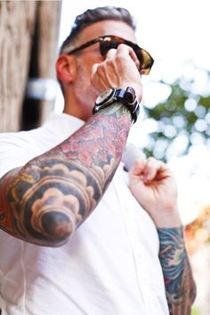 a man with tattoos on his arm drinking from a cup while wearing sunglasses and looking off to the side