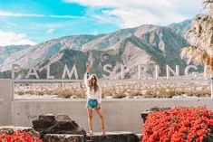 a woman standing in front of palm springs sign with her arms up and hands raised