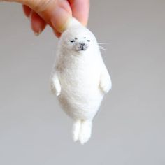 a small white stuffed animal being held by a person's hand with their fingers