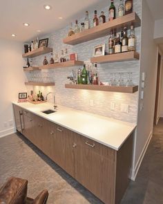 a kitchen with shelves filled with bottles and glasses on top of the countertop, next to a leather chair