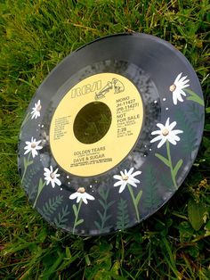 a record sitting in the grass with daisies painted on it's side and bottom