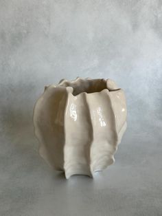 a white ceramic vase sitting on top of a gray table next to a grey wall