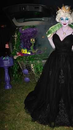 a woman in a black dress standing next to a car with green decorations on it