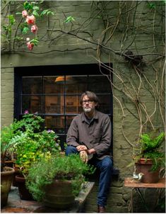 a man sitting on a window sill surrounded by potted plants