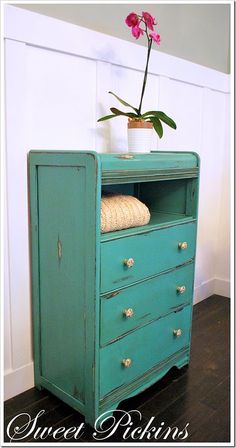 a green dresser with a flower on top and a potted plant in the corner