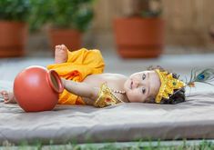 a baby laying on its back next to a red ball and some potted plants