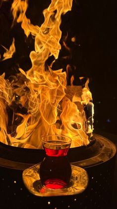 a glass filled with liquid sitting on top of a table covered in fire and flames