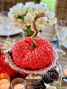 a red pumpkin sitting on top of a glass plate next to pine cones and candles