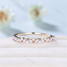 an image of a wedding ring with opal stones on it's side and flowers in the background