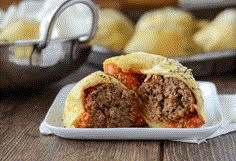 a meatball roll on a plate with other rolls in the background and one half eaten