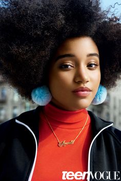 a woman with an afro and blue pom - poms on her ear is looking at the camera