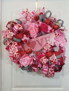 a valentine's day wreath with the word love on it and pink flowers in front of a white door