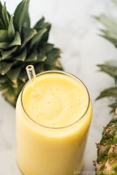 a glass filled with yellow liquid next to a pineapple