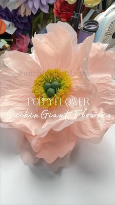 a large pink flower sitting on top of a white table next to other colorful flowers