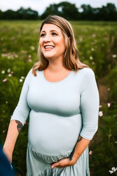 a pregnant woman smiles while standing in a field