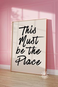 this must be the place sign in front of a pink wall with wooden flooring