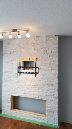 an empty room with a brick fireplace and tv mounted on the wall, in front of two recessed lights