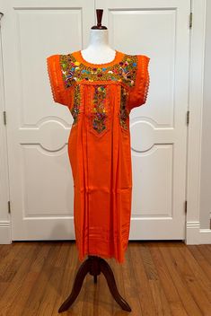 Mexican orange dress is made with hand embroidery and multicolor silk threads by Zapotecs from Oaxaca Mexico. APPROXIMATE MEASUREMENTS. Around bust 48" Shoulder to bottom hem 44" PC # B-833 Made With 100% hand embroidery. 100% Artisanal Made. Imported Made in Oaxaca Mexico No two are alike-different embroidery patterns/colors Handmade, Boho, bohemian, Mexico, Hippie, Embroidery, Vintage, Huipil, Tunic, One of A Kind. Artisan Made, Ethnic Floral, Vintage Style. Orange Embroidered Summer Dress, Orange Embroidered Short Sleeve Dress, Orange Embroidered Bohemian Dress, Orange Bohemian Embroidered Dress, Traditional Orange Beach Dress, Orange Short Sleeve Dress For Festivals, Short Sleeve Orange Dress For Festival, Orange Embroidered Fitted Dress, Fitted Orange Embroidered Dress