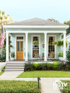 a blue house with white trim and pillars on the front porch, surrounded by greenery