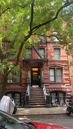 an apartment building with stairs leading up to the front door and trees lining the street