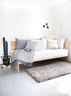 a bed with pillows and blankets on it in a room next to a cactus plant