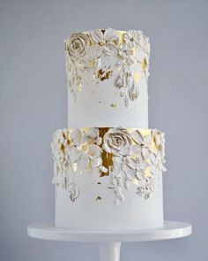 a three tiered cake with white frosting and gold flowers on the bottom layer