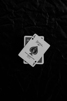 two playing cards sitting on top of each other in front of a black cloth background