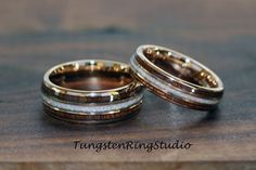 two wedding bands with gold and white inlays are on top of a wooden surface