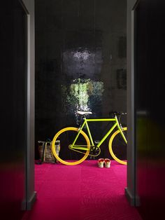 a yellow bicycle is parked in front of a pink carpeted room with black walls