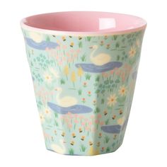 a cup that is sitting on top of a white surface with flowers and birds in the background