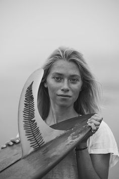 black and white photograph of a woman holding a surfboard in front of her face