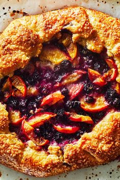 a pie with blueberries and peaches on it sitting on top of a piece of parchment paper