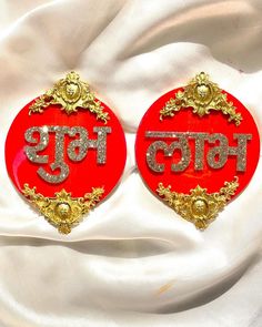 pair of red and gold earrings with the word india in two languages on it, sitting on a white cloth