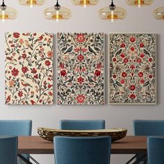 a dining room table with blue chairs and two paintings on the wall above it that have red flowers