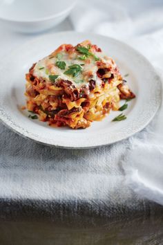 a white plate topped with lasagna covered in cheese and sauce on top of a table