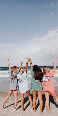 four girls standing on the beach with their arms in the air